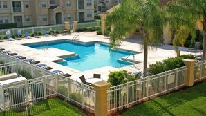 Una piscina rectangular con cerramiento blanco, rodeada de sillas de descanso y palmeras.