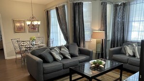 Una sala de estar moderna con dos sofás grises, una mesa de centro de vidrio y un comedor con una silla y una mesa de metal.