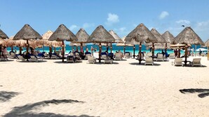 A beach with thatched umbrellas and lounge chairs.