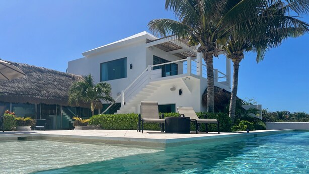 A modern resort with a swimming pool, palm trees, and a thatched-roof building.