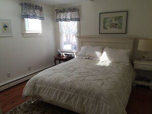 A bedroom with a large bed, a bedside table with a lamp, a small table with a lamp, and a framed picture on the wall.