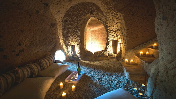 A cozy, dimly lit room with a stone interior, a wooden bench, and candles providing a warm ambiance. - A unique luxury home, designer interiors, in a fairytale town (Civita di Bagnoregio)