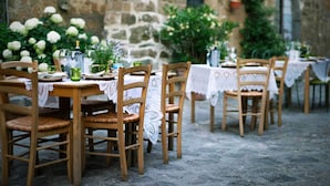An outdoor dining area with wooden tables and chairs, lace tablecloths, and greenery in the background. - A unique luxury home, designer interiors, in a fairytale town (Civita di Bagnoregio)