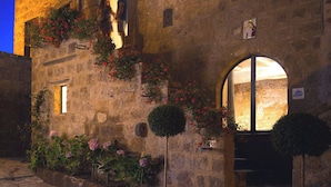 A stone building with arched windows and a door, surrounded by potted plants and flowers. - A unique luxury home, designer interiors, in a fairytale town (Civita di Bagnoregio)