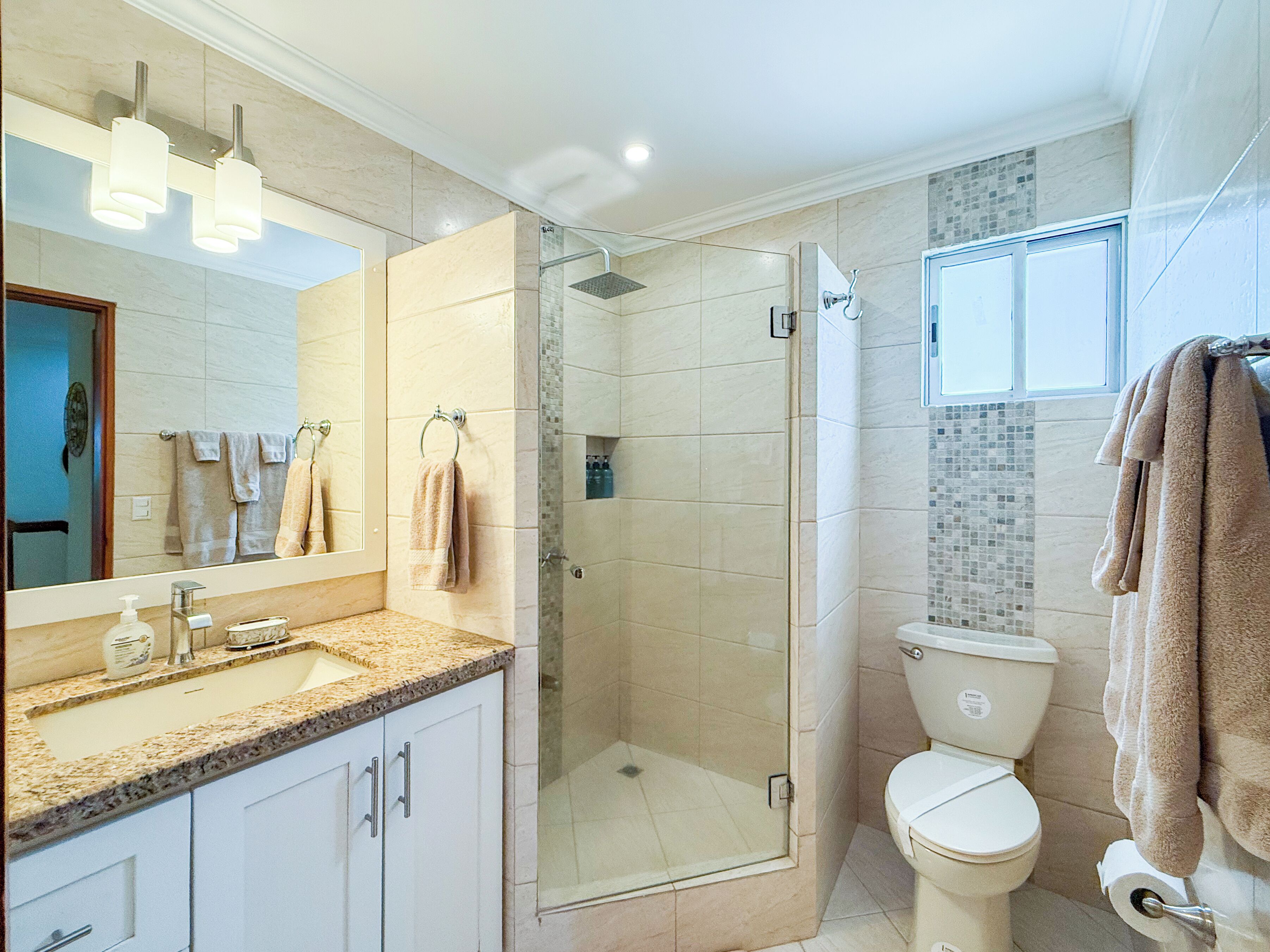 A modern bathroom with a glass-enclosed shower, a toilet, and a sink with a marble countertop.