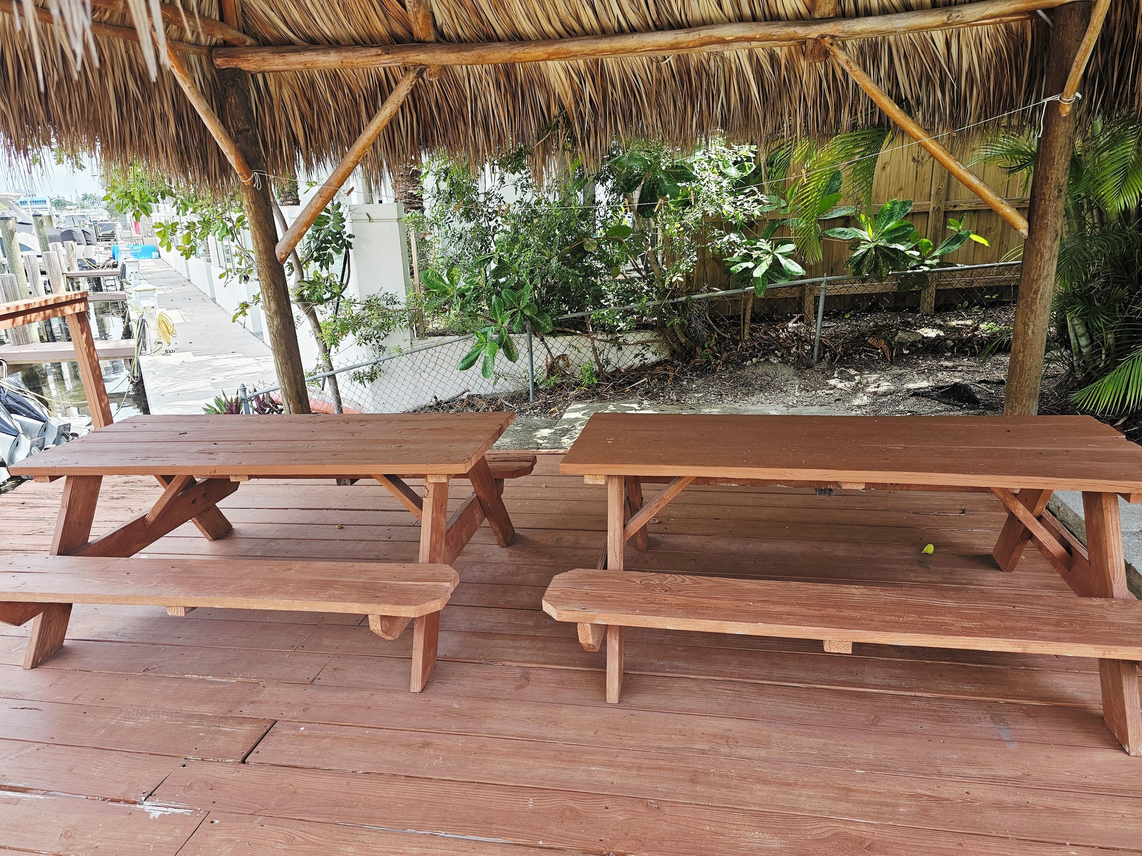 A wooden deck with picnic tables under a thatched roof.