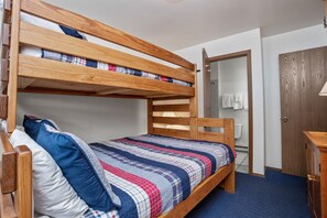 Un lit superposé avec une couverture à carreaux, une tête de lit en bois et un tapis bleu.