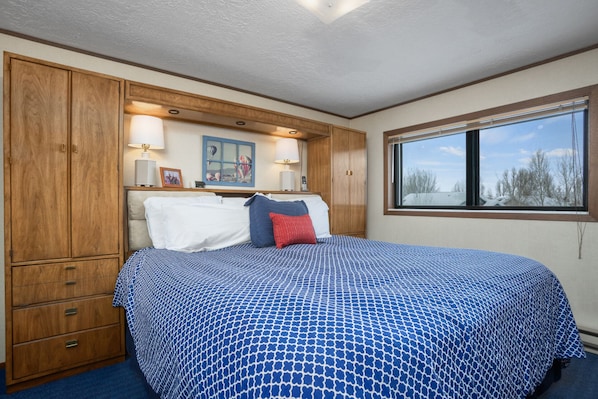 A bedroom with a bed, wooden wardrobe, and a window with a view.