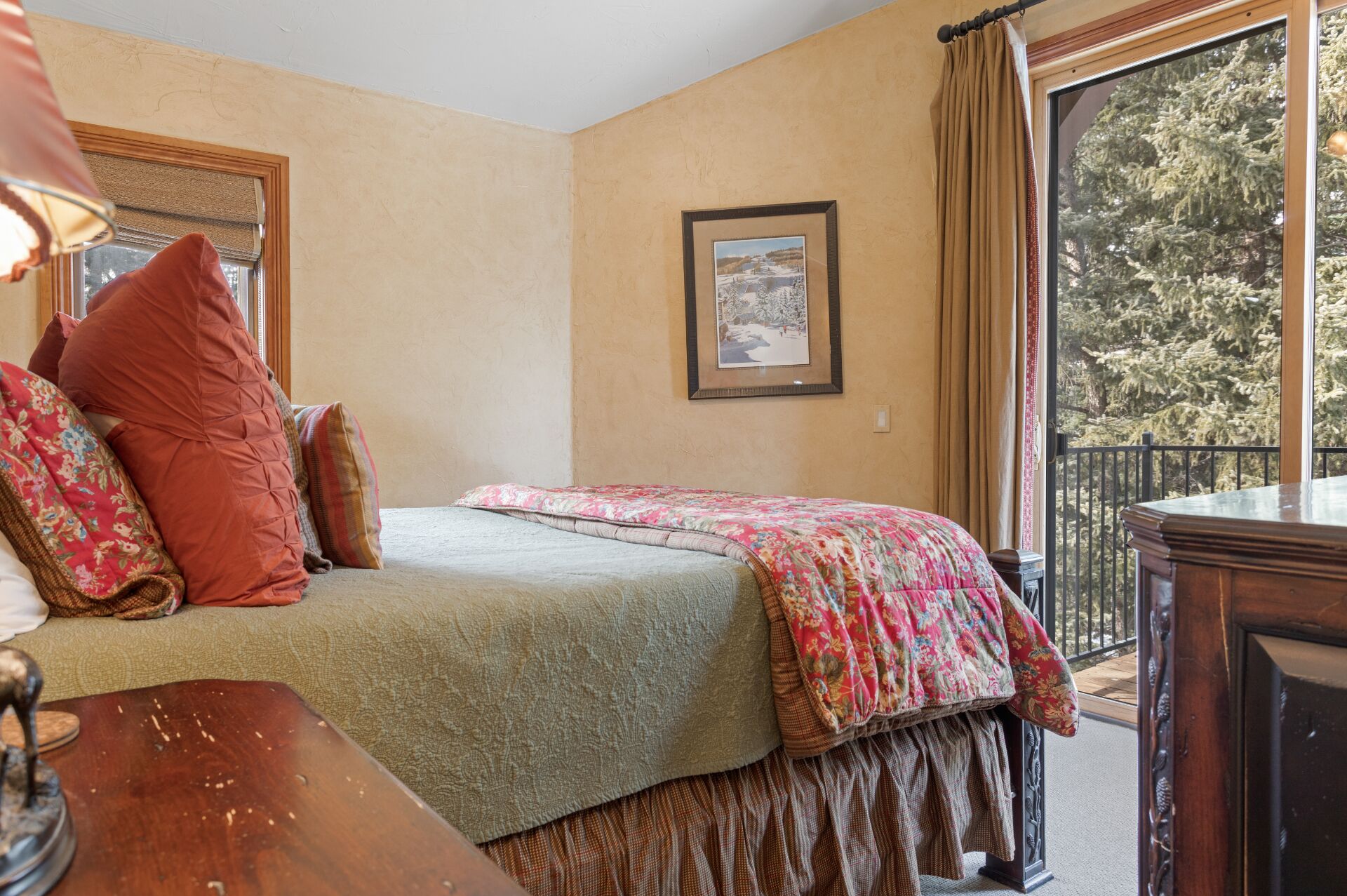 A bedroom with a bed, pillows, a framed picture, and a view of trees through a window.