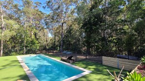 A rectangular swimming pool with a surrounding green lawn and a wooden deck.