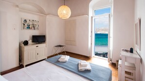 A bedroom with a bed, a TV on a cabinet, a towel rack, and a view of the sea through an open door. - Mykonos Old Harbor Front Suite with Balcony  (Mikonos)