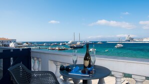 A balcony with a table featuring a bottle of wine, glasses, and sunglasses. The view includes a marina with various boats and a cruise ship in the background. - Mykonos Old Harbor Front Suite with Balcony  (Mikonos)