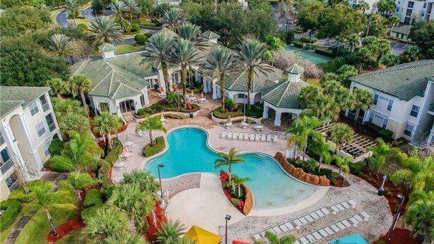 Vista aérea de un complejo turístico con una piscina central, rodeado de palmeras y varios edificios.
