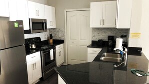 Una cocina moderna con gabinetes blancos, un refrigerador de acero inoxidable, un microondas, una estufa y un lavamanos.
