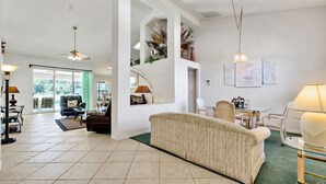 A spacious living room with a sofa, chairs, a dining table, and a staircase leading to an upper level. - Secluded Luxury Pool Home, Close to Disney w/ Oversized pool  Special offers now (Kissimmee)