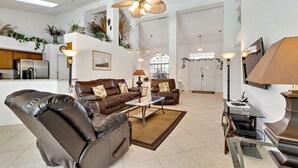 A spacious living room with leather sofas, a glass coffee table, and a ceiling fan. - Secluded Luxury Pool Home, Close to Disney w/ Oversized pool  Special offers now (Kissimmee)