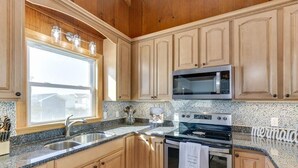 A kitchen with wooden cabinets, a granite countertop, a stainless steel sink, a microwave, and an oven. - OCS4 Semi-Ocean-Front Home with Gorgeous Views (Nags Head)