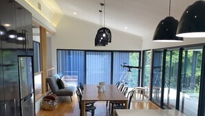 A modern kitchen with a dining area, large windows, and a view of the outdoors. - Escarpment - Bush to beach views (Berry)