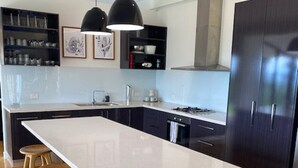 A modern kitchen with a central island, bar stools, dark cabinetry, and stainless steel appliances. - Escarpment - Bush to beach views (Berry)