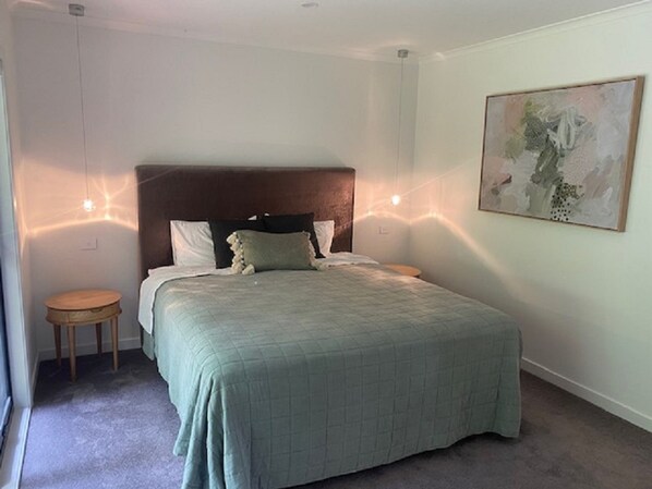 A bedroom with a large bed, a headboard, two bedside tables, and a painting on the wall. - Escarpment - Bush to beach views (Berry)
