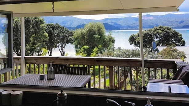Un balcone con tavolo e sedie in legno, affaccio su un lago e montagne.