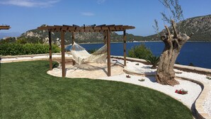 Eine Hängematte unter einer Holzpergola am See mit Bergkulisse.