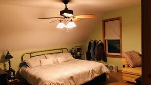 Ein Schlafzimmer mit einem Bett, einem Deckenventilator, einem Fenster und einem Nachttisch mit Lampe.
