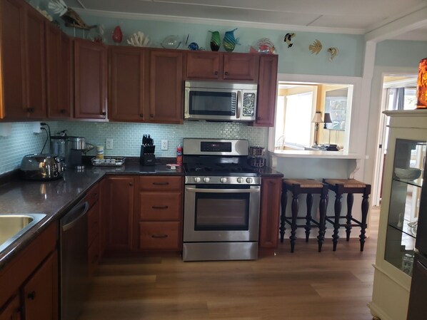 A kitchen with wooden cabinets, a microwave, an oven, and a sink. There are decorative items on the wall and a window with a view.