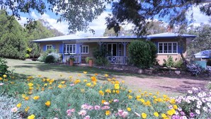 A two-story house with a blue roof, a front porch, and a garden with yellow and pink flowers.