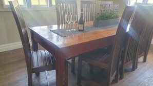 A dining table with six chairs, a bottle of wine, and two wine glasses on a wooden table with a woven placemat.