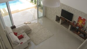 Una sala de estar moderna con un sofá blanco, un televisor de pantalla plana grande y vista a una piscina a través de puertas de vidrio.