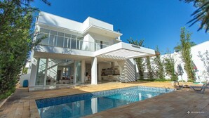 Una casa moderna de dos pisos con piscina, mobiliario exterior y un patio cubierto.