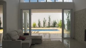 Una sala de estar moderna con un amplio ventanal que da a un espacio exterior con piscina y vegetación.