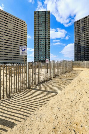 Un sentier sablonneux mène à une zone délimitée par une barrière, où un panneau indique l’emplacement d’une plage.