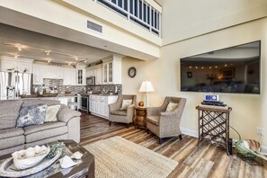 A spacious living area with a high ceiling, a kitchen with white cabinetry, and a flat-screen TV mounted on the wall. - XPLORIE ACTIVITIES & LINENS INCLUDED*! One of the most luxurious penthouse condos in Ocean City. Completely renovated with spectacular and breathtaking 2-story views of Ocean, Bay, and MD/DE coastline to Bethany. (Ocean City)