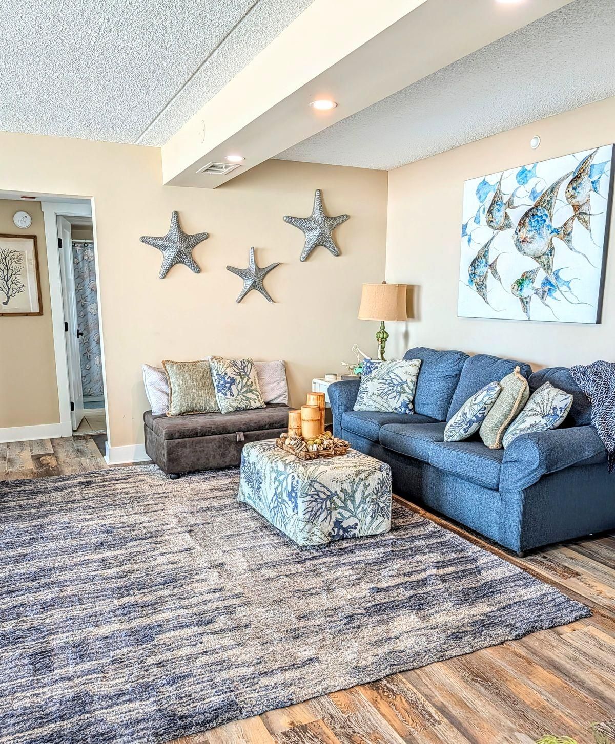 A living room with a blue sofa, a brown ottoman, and a patterned rug.
