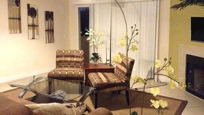 Ein Wohnzimmer mit einem Glastisch, zwei gemusterten Sesseln, einer Couch und einem Kamin.