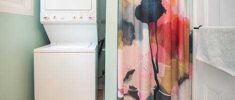 Een wasruimte met een voorlader wasmachine en droger, een kleurrijk douchegordijn en een handdoekrek.
