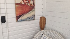 A wicker chair with a dark cushion and a striped pillow against a white wall with a vintage 'Welcome to Williams Bay, Wisconsin' sign. - 3 BR/2 BA House just steps from Lake Geneva (Williams Bay)