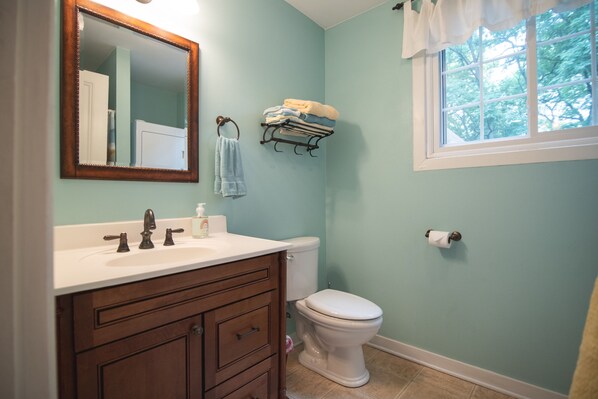 A bathroom with a white sink, wooden vanity, a toilet, and a window with a view of trees.