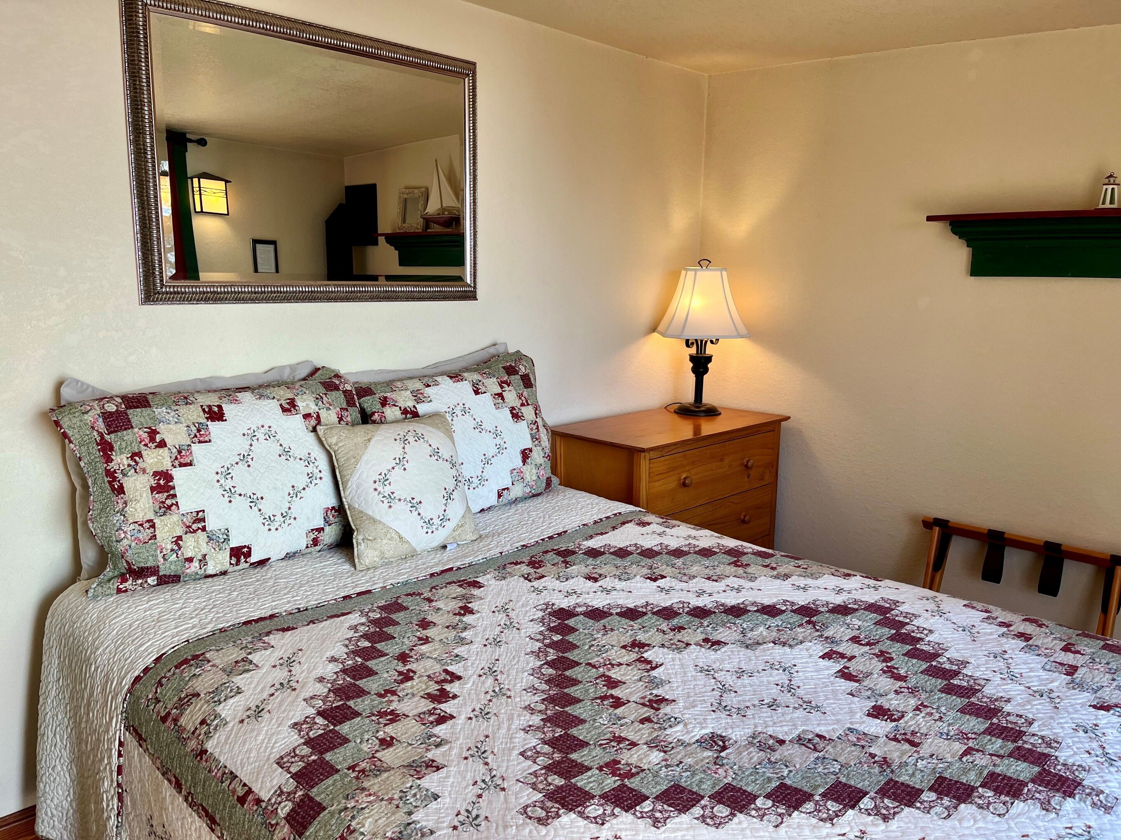 A bedroom with a bed, a dresser, a mirror, and a lamp.