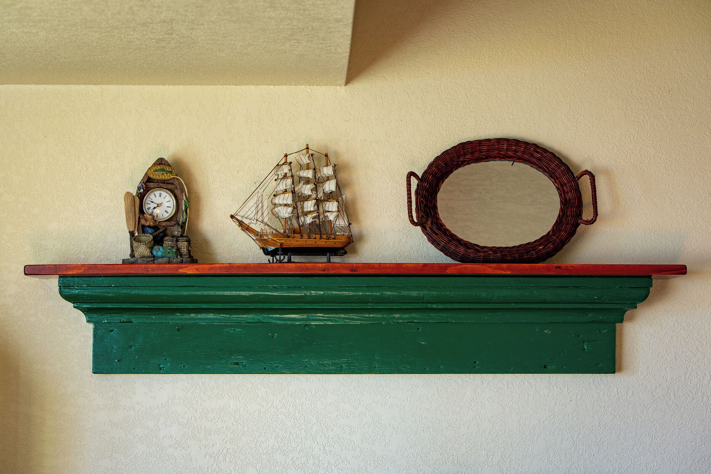 A shelf with a clock, a ship model, and a circular mirror.