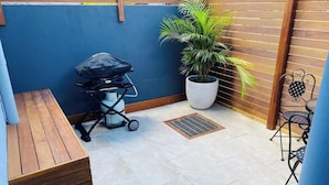 A small patio area with a wooden bench, a stroller, a potted plant, and a metal chair. - Unit 6 - Modern Studio Huskisson main street By Nautilus Apartments Jervis Bay (Huskisson)