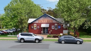 A red building with a sign reading "HUSKISSON PICTURES" and a white car parked in front. - Unit 6 - Modern Studio Huskisson main street By Nautilus Apartments Jervis Bay (Huskisson)