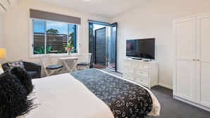 A bedroom with a bed, a TV, a wardrobe, and a window with a view. - Unit 6 - Modern Studio Huskisson main street By Nautilus Apartments Jervis Bay (Huskisson)