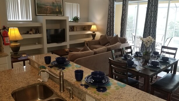 Een moderne woonkamer met een bank, een eettafel gedekt met blauw servies, een televisie en een open haard.
