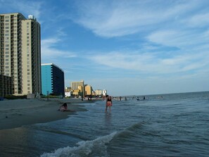 A beach with a high-rise building, a pier, and people enjoying the water. - Beautiful Cottage w/ Pool, Steps to Beach, Free WiFi and parking (Myrtle Beach)