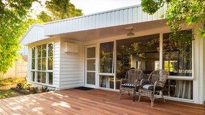 A covered outdoor deck with wooden flooring and wicker furniture. - Spirit Level Mallacoota (Mallacoota)