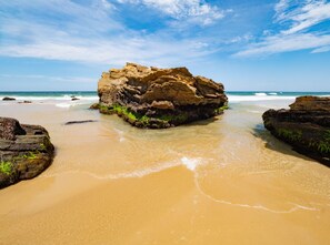 Formação rochosa rodeada por uma praia de areia sob um céu azul límpido.