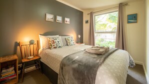 A bedroom with a bed, bedside table, lamp, and a window with curtains. - Spirit Level Mallacoota (Mallacoota)